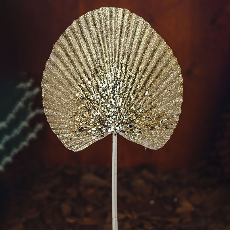 No centro, folha de latania banhada em glitter dourado com haste em fundo marrom escuro