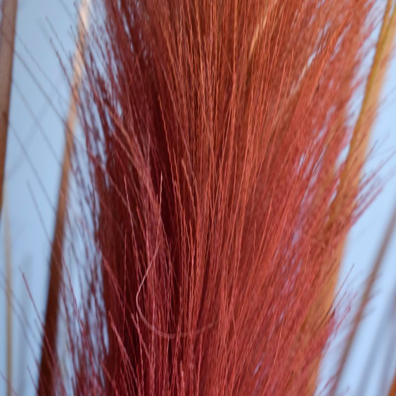 Foco aproximado e detalhado das plumas artificiais na cor marsala em fundo azul