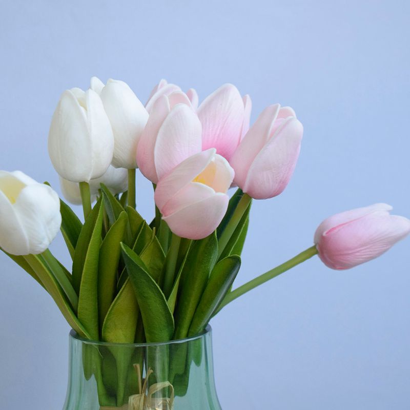 No lado esquerdo buquê de tulipas rosas claro e brancas em vaso de vidro transparente em fundo azul