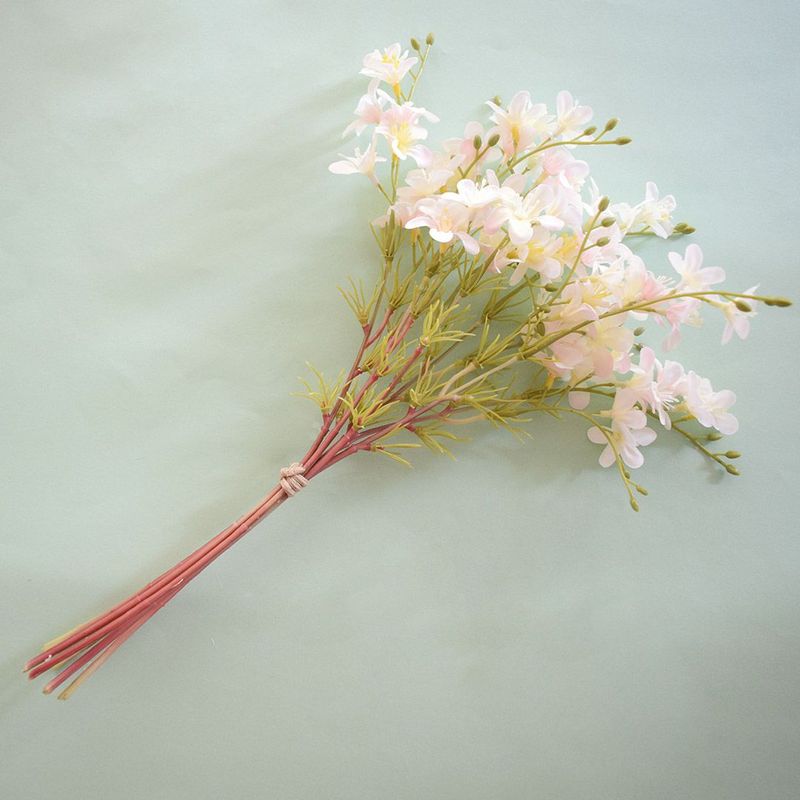Na diagonal para direita, buquê artificial  flor do campo rosa claro  em fundo azul