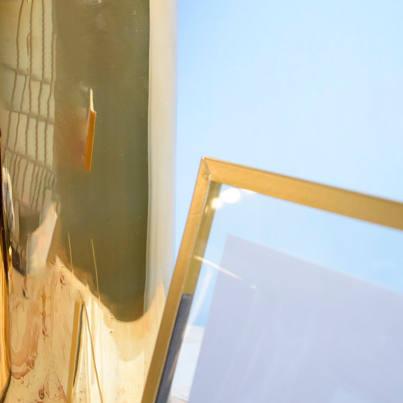 Foco aproximado no canto superior esquerdo do porta retrato com paspatur em vidro e moldura metalica dourada em fundo azul
