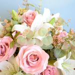 No centro, arranjo de rosas e lirios artificiais brancos e rosa claro com folhagem de eucalipto em fundo azul