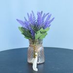 No centro, arranjo artificial de lavanda em vaso de vidro ambar com pingente sobre mesa redonda preta em fundo azul
