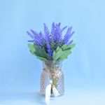 No centro,  arranjo artificial de lavanda em vaso de vidro ambar com pingente em fundo azul