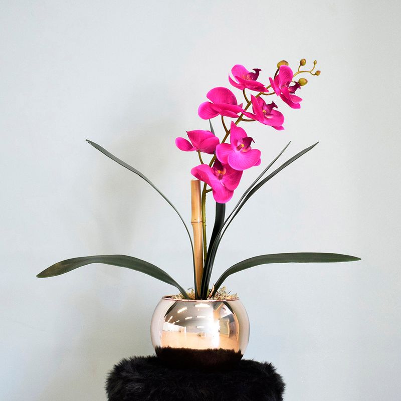 No centro, arranjo de orquidea artificial pink 3D no vaso redondo rose gold sobre mesa lateral redonda preta em fundo azul