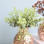 No centro, foco aproximado e detalhado do arranjo de eucalipto no vaso tipo moringa em vidro espelhado rose em fundo azul
