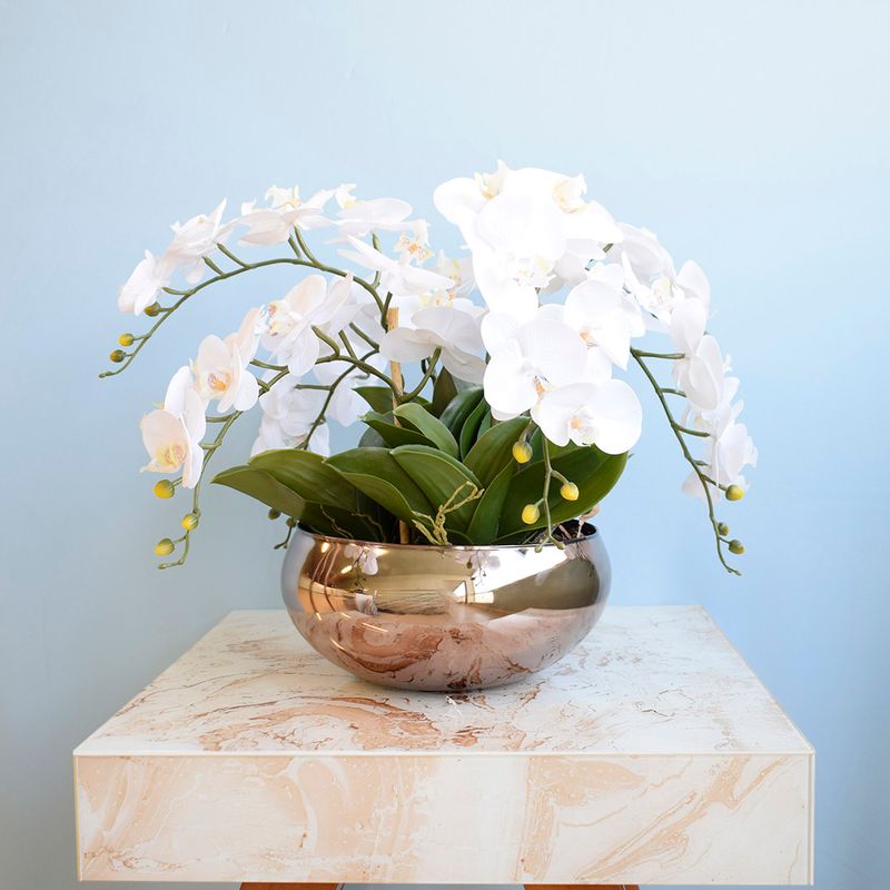 Arranjo composto por seis hastes de orquídea branca em vaso de redondo de vidro espelhado bronze em fundo azul